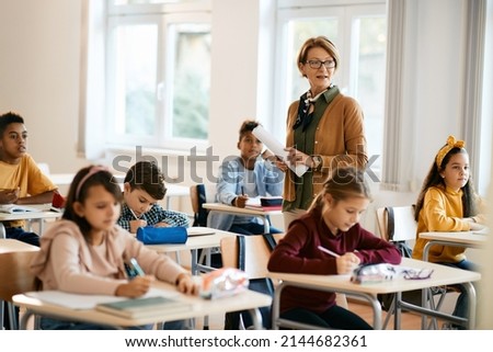 Mature teacher holding a class to group of school kids at primary school. Royalty-Free Stock Photo #2144682361