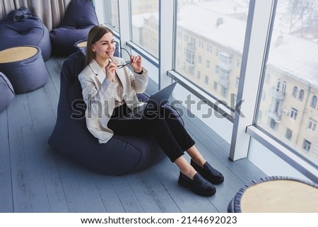 Successful woman in casual wear is typing on a netbook while working on a new project while sitting at a desk in a modern workspace. Business lady in a jacket and glasses. Telework