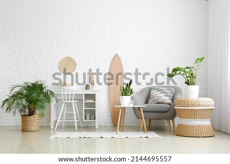 Interior of light living room with wooden surfboard, workplace and houseplants