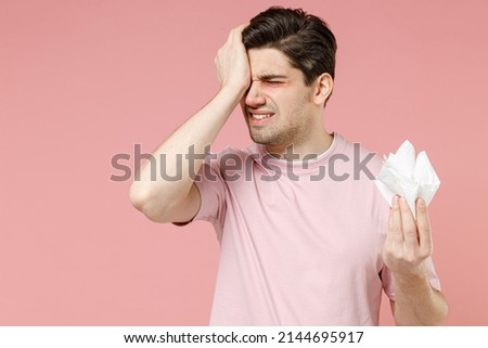 Unhealthy sick allergic crying man has watery swelling red eyes runny nose suffer from allergy symptoms hay fever hold paper napkin isolated on pastel pink color background studio. Seasonal rhinitis Royalty-Free Stock Photo #2144695917