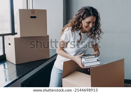 Spanish girl in white t-shirt packing books. Carefree young european woman unpacking boxes. Cheerful student goes to university. Relocation and independence concept. Royalty-Free Stock Photo #2144698913