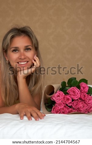 Blonde with a snow white smile rejoices in a delightful bouquet of roses from a loved one, presented for a wedding anniversary. A tanned girl poses in a room close up with a bouquet of pink roses