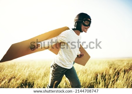 Ready for lift off. Shot of a young boy pretending to fly with a pair of cardboard wings in an open field. Royalty-Free Stock Photo #2144708747
