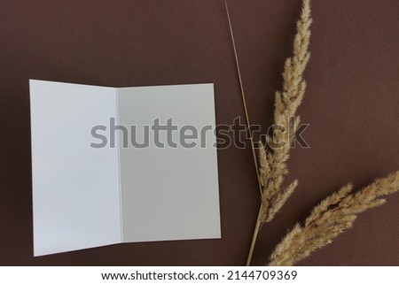 Blank paper with copy space , dry grass on dark brown background  top view. Card mockup,Greetings, wedding invitations blank, paper sheet.  
