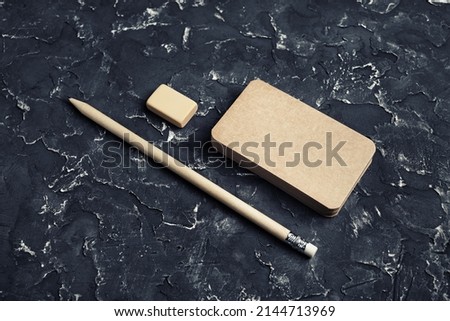 Photo of blank kraft business card, pencil and eraser on black plaster background.