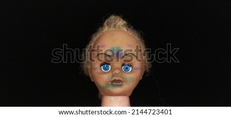 Scary, evil, spooky, demonic and possessed killer baby child girl doll head with creepy face and blue eyes on island of dead dolls during dark black night background with copy space. Closeup side view