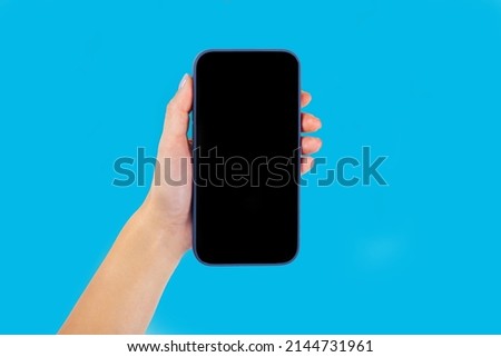 A modern smartphone with a blank screen for a layout in the hands on a blue background, top view with free space
