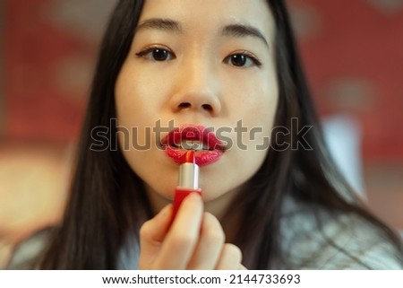 close-up on face of beautiful asian woman putting red lipstick on her lips - focus on mouth
