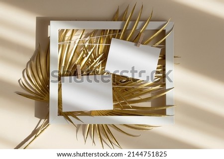 Two invitation card mockup with golden palm leaves in white frame on beige pastel background. Top view, flat lay, copy space. Template blank of white paper mock up for branding and advertising