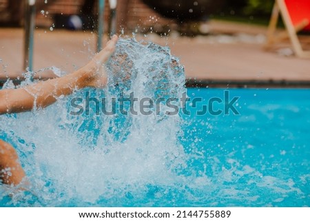 Kid's legs splashing water in blue swimming pool. Focus is at the splashing. Summertime. Royalty-Free Stock Photo #2144755889