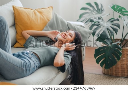 Happy woman relaxing in her sofa at home, Smiling girl is listening to music with headphones and lying down with eyes closed, Enjoy good quality sound, Stress free concept. Royalty-Free Stock Photo #2144763469