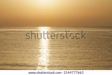 Silhouettes of man and woman kayaking in the sea at sunrise.