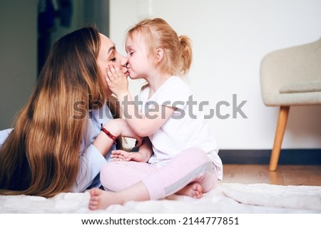 Happy family. Young mom kissing her cute little daughter at home lying on the floor
