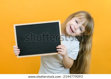 girl holding a board sheet. Cute little girl with chalk board. yellow background. copy space. place for your text