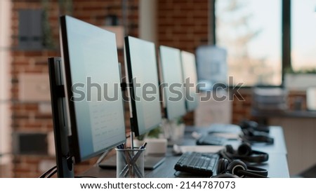 Nobody at customer care workstation with multiple computers used by telemarketing agents to give support to clients at call center helpline. Empty desks with monitors and headphones. Royalty-Free Stock Photo #2144787073