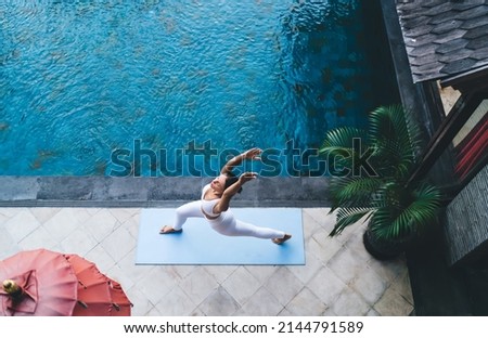 Flexible woman practice balance asana raising hands breathing at pool terrace, top view on fit girl doing stretching exercises during morning workout for feeling vitality and keeping healthy lifestyle