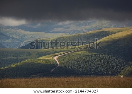 Rainy gloomy sky on the background of the line of mountains, close-up. The sun's rays make their way onto the surface of the earth and the road
