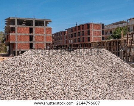 A hill of gray rubble against the background of buildings under construction.