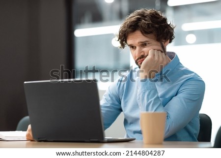 Portrait of sad bored business man sitting at desk using pc, leaning head on hand looking at screen. Upset stressed guy suffering job problems, reading bad negative news at office, free copy space Royalty-Free Stock Photo #2144804287