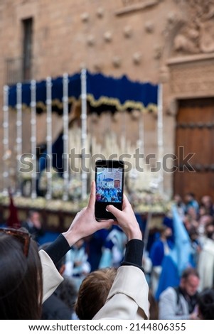 Caucasian woman taking photos and videos with her mobile phone of the Holy Week processions in Salamanca, Spain.