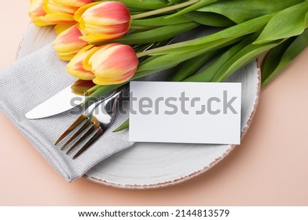 Festive table setting with a card and bouquet of tulips on a beige background. Mockup
