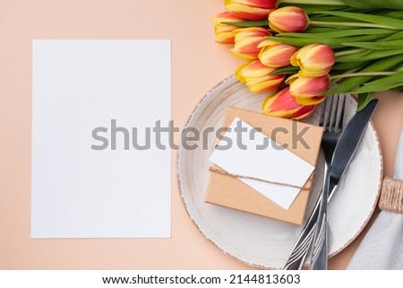 Mockup menu card. Top view of table setting with menu card, present, cutlery and fresh tulips for festive dinner.