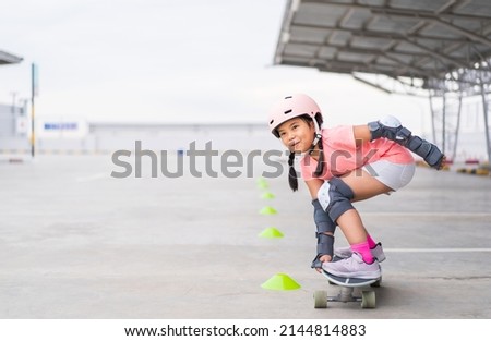 asian child or kid girl playing surf skate or skateboard and crouching with turning practice cones in skating rink or sports park at parking to wearing safety helmet elbow pads wrist and knee support Royalty-Free Stock Photo #2144814883