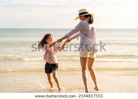 Happy Asian family on beach vacation. Mother and little daughter walking and playing together on tropical beach at summer sunset. Mom and child girl kid enjoy and fun outdoor lifestyle on the beach Royalty-Free Stock Photo #2144817555