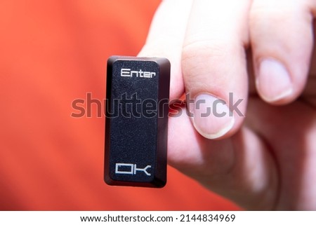 Close-up of a man's hand with a button from a keyboard. Plastic button with the inscription ENTER.