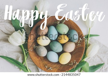 Happy Easter greeting card. Happy Easter text and stylish Easter eggs in wooden plate, tulips, linen napkin on rustic table, flat lay. Seasons greeting card, handwritten lettering