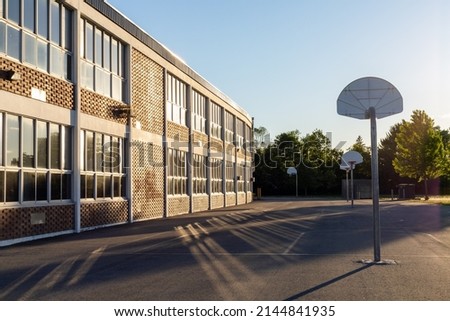 Schoolyard with basketball court and school building exterior in the sunny evening. School yard with playground Royalty-Free Stock Photo #2144841935