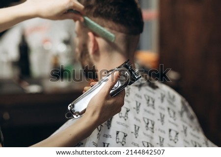 a hairdresser cuts a bearded young guy with a hair trimmer, combing the hair on his head. Work of the master in men's haircut in a barbershop Royalty-Free Stock Photo #2144842507