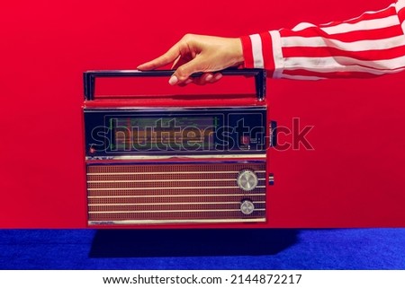 Retro radio. Female hand holding, touching radioreceiver isolated on blue and red background. Vintage, retro 80s, 70s style. Complementary colors. Concept of fashion, art, creativity, ad, sales