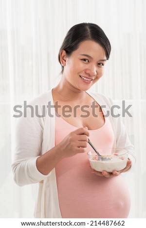 Pregnant Vietnamese woman eating muesli with milk for breakfast