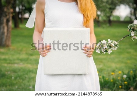 A photo book in a white leather cover in the hands of a woman in spring near a flowering branch of an apple tree