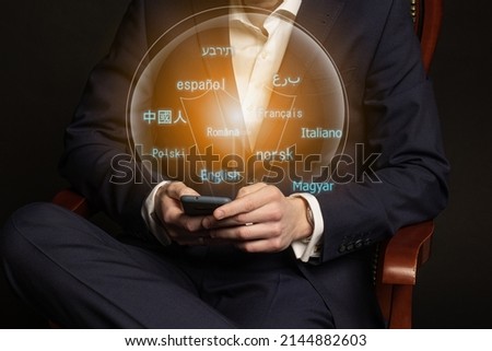 E-learning. Closeup businessman hands at work desk using mobile phone with creative grid of digital neon digital languages on blurred background.