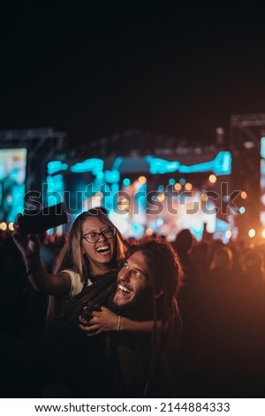 Romantic couple having fun on a music festival and using smartphone while posing for a selfie. Love and celebration concept.