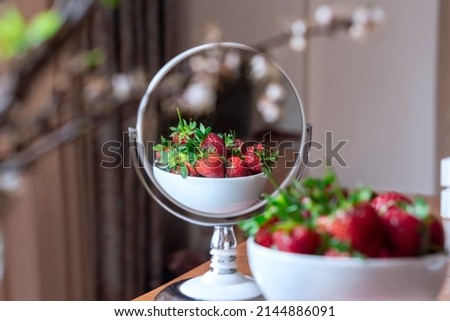 A bowl of red strawberries reflected on a mirror on a wooden table, close up, still life photography