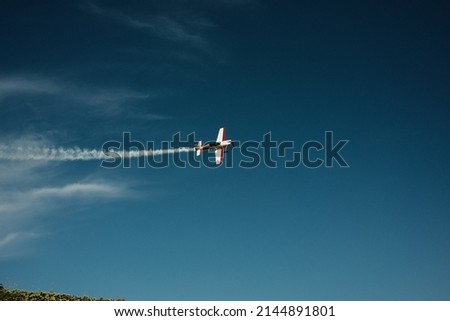  A small plane maneuvers in a blue sky with a contrail. High quality photo