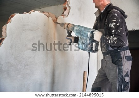 Close up of special powerful hand instrument with percussion mechanism for drilling and breaking walls. Man holding jackhammer and dismantling inner wall in room. Royalty-Free Stock Photo #2144895015