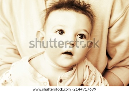 Surprised infant baby boy with big blue eyes and disheveled hair, sepia. Portrait of a frightened child with a messy hairstyle, black and white