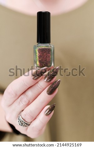 Female hand with long nails and a bottle of green brown nail polish