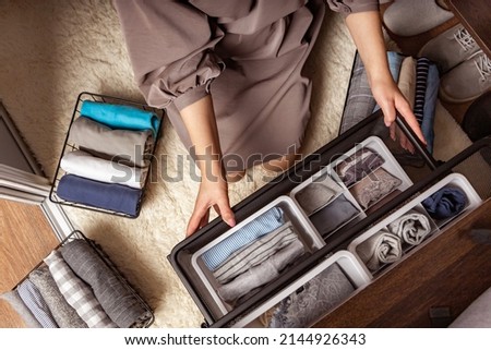 Housewife hands with neatly put underwear, clothes and accessories modern wardrobe organization top view. Woman arms carrying ecological minimalist clothing box container storage Marie Kondo method