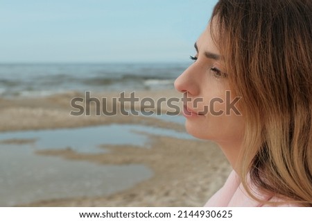 A young beautiful woman in a pink coat stands on the sea or ocean shore with a cup of coffee and enjoys the view. brunette on the seashore drinking coffee. glass with coffee.