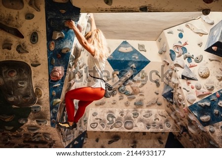 Climber wearing in climbing equipment. Practicing rock-climbing on a rock wall indoors. Xtreme sports and bouldering concept.