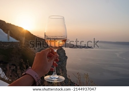 Hand holding a glass of a rose wine with a view to Santorini caldera. Royalty-Free Stock Photo #2144937047