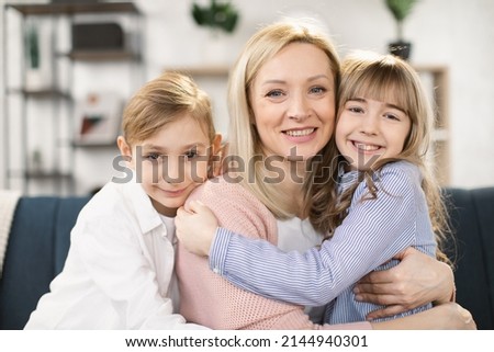 Portrait of happy mother hugging two little kids. Joyful affectionate mom cuddling sweet sibling son and daughter, looking at camera with toothy smile. Family relationship, motherhood. Head shot