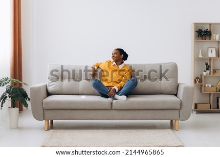 Young black lady enjoying weekend and relaxing on comfortable couch at home. African American woman sitting on sofa in living-room, stretching arms and smiling feeling untroubled and happy, back view Royalty-Free Stock Photo #2144965865