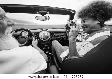 Happy senior couple having fun in convertible car during summer vacation - Focus on woman hand holding vintage camera