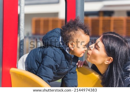 dark-haired woman and cute little boy with black curly hair kissing looking each other on a slide medium shot outdoor. High quality photo